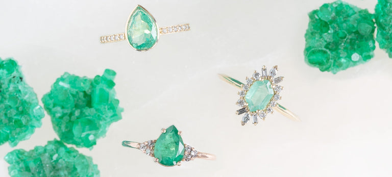 three emerald gemstone engagement rings on white marble surface