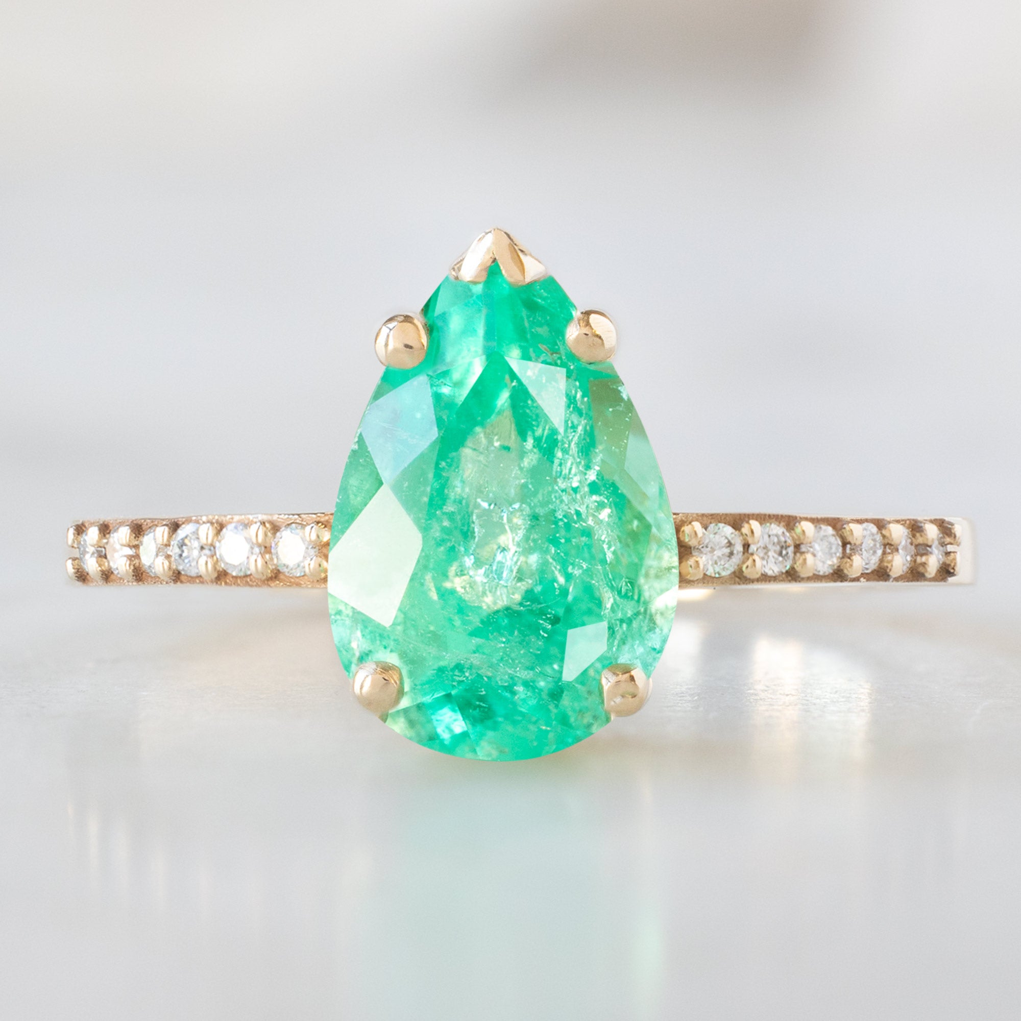 The Willow Ring with a 1.47ct Pear Emerald in 14K Yellow Gold on White Marble